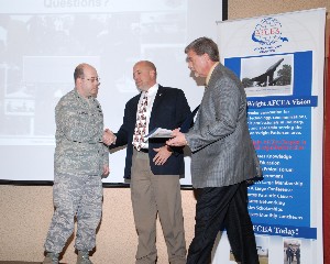 Col. Michael J. Stinson, USAF (l), commander, 88th Communications Group, 88th Air Base Wing, Aeronautical Systems Center, Air Force Materiel Command, Wright-Patterson Air Force Base, Ohio, receives a token of appreciation from Hart (c) and McCombs at the May luncheon.